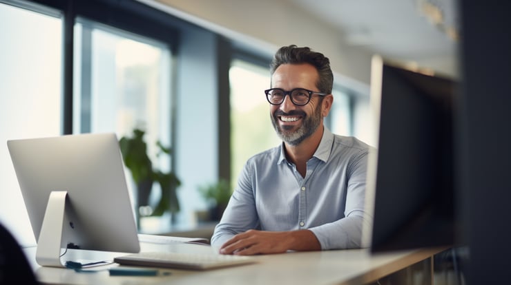 Wide shot of a smiling and confident professional man in his 40s, looking at the computer screen, in a modern office